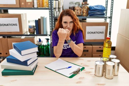 Photo for Young redhead woman wearing volunteer t shirt at donations stand ready to fight with fist defense gesture, angry and upset face, afraid of problem - Royalty Free Image