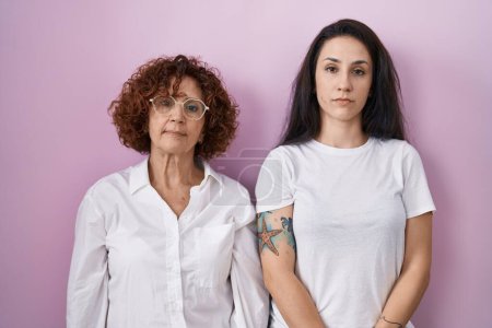 Photo for Hispanic mother and daughter wearing casual white t shirt over pink background relaxed with serious expression on face. simple and natural looking at the camera. - Royalty Free Image