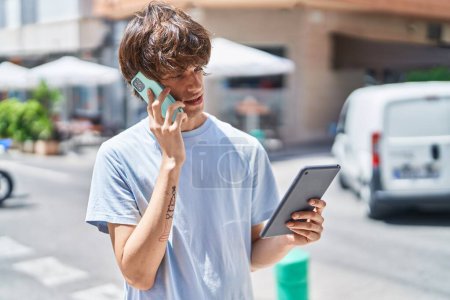 Téléchargez les photos : Jeune homme blond parlant sur smartphone en utilisant le pavé tactile à la rue - en image libre de droit