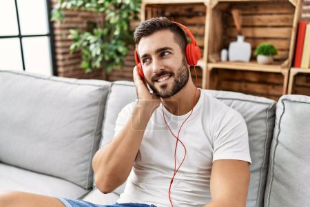 Téléchargez les photos : Jeune homme hispanique souriant confiant écoutant de la musique à la maison - en image libre de droit