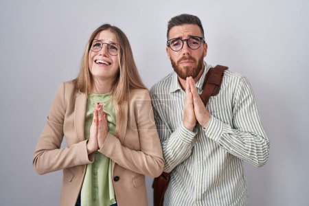 Foto de Young couple standing over white background begging and praying with hands together with hope expression on face very emotional and worried. begging. - Imagen libre de derechos