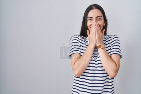 Photo for Young brunette woman wearing striped t shirt laughing and embarrassed giggle covering mouth with hands, gossip and scandal concept - Royalty Free Image
