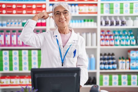 Photo for Middle age woman with tattoos working at pharmacy drugstore smiling pointing to head with one finger, great idea or thought, good memory - Royalty Free Image