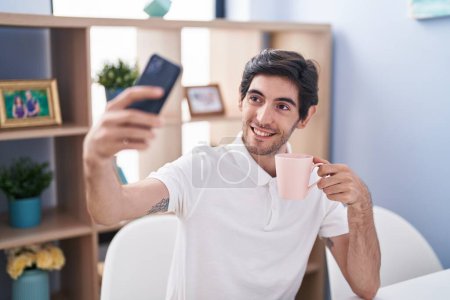 Photo for Young hispanic man making selfie by smartphone drinking coffee at home - Royalty Free Image
