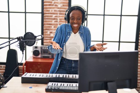 Téléchargez les photos : Belle femme noire jouant du piano au studio de musique célébrant la réalisation avec un sourire heureux et l'expression gagnante avec la main levée - en image libre de droit