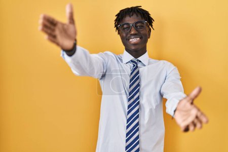 Téléchargez les photos : African man with dreadlocks standing over yellow background looking at the camera smiling with open arms for hug. cheerful expression embracing happiness. - en image libre de droit