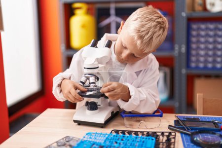 Téléchargez les photos : Adorable enfant en bas âge utilisant un microscope debout en classe - en image libre de droit