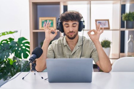 Téléchargez les photos : Homme arabe avec la barbe travaillant à la radio se détendre et sourire les yeux fermés en faisant geste de méditation avec les doigts. concept de yoga. - en image libre de droit