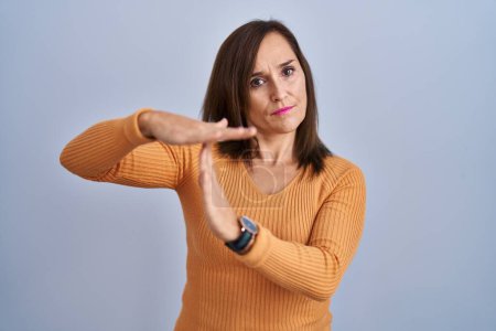 Téléchargez les photos : Middle age brunette woman standing wearing orange sweater doing time out gesture with hands, frustrated and serious face - en image libre de droit
