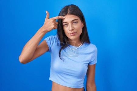 Photo for Brunette young woman standing over blue background pointing unhappy to pimple on forehead, ugly infection of blackhead. acne and skin problem - Royalty Free Image