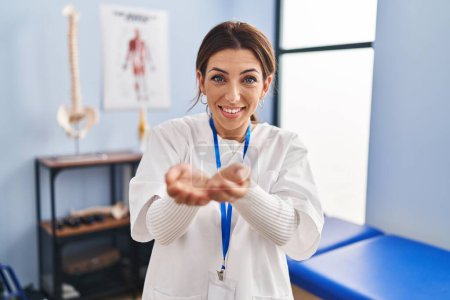 Photo for Young brunette woman working at pain recovery clinic smiling with hands palms together receiving or giving gesture. hold and protection - Royalty Free Image