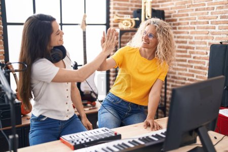 Photo for Two women musicians high five with hands raised up at music studio - Royalty Free Image