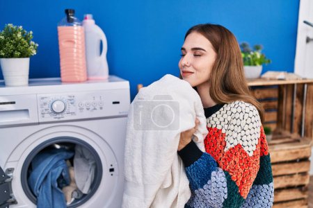 Foto de Mujer joven oliendo toalla lavando ropa en la lavandería - Imagen libre de derechos