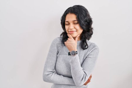 Photo for Hispanic woman with dark hair standing over isolated background looking confident at the camera smiling with crossed arms and hand raised on chin. thinking positive. - Royalty Free Image