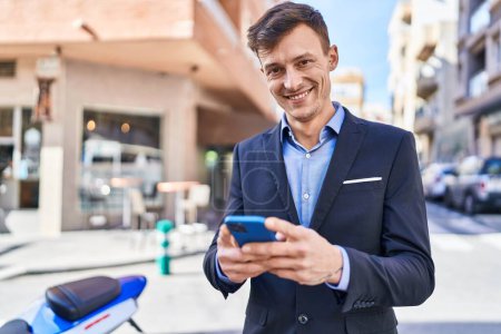 Téléchargez les photos : Jeune homme d'affaires travailleur souriant confiant en utilisant smartphone à la rue - en image libre de droit