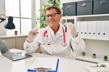 Photo for Senior doctor man holding syringe and blood sample winking looking at the camera with sexy expression, cheerful and happy face. - Royalty Free Image