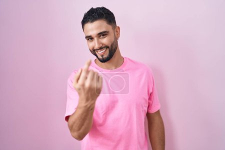 Photo for Hispanic young man standing over pink background beckoning come here gesture with hand inviting welcoming happy and smiling - Royalty Free Image