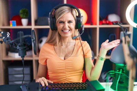 Téléchargez les photos : Young woman playing video games smiling cheerful presenting and pointing with palm of hand looking at the camera. - en image libre de droit