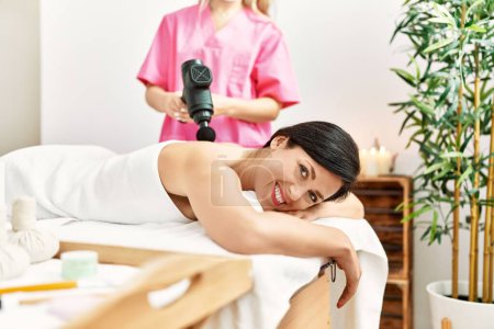 Téléchargez les photos : Middle age hispanic woman smiling confident having back massage using percussion pistol at beauty center - en image libre de droit