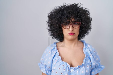 Foto de Young brunette woman with curly hair wearing glasses over isolated background skeptic and nervous, frowning upset because of problem. negative person. - Imagen libre de derechos