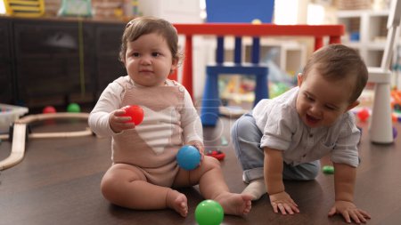 Téléchargez les photos : Deux tout-petits jouant avec des boules assises sur le sol à la maternelle - en image libre de droit