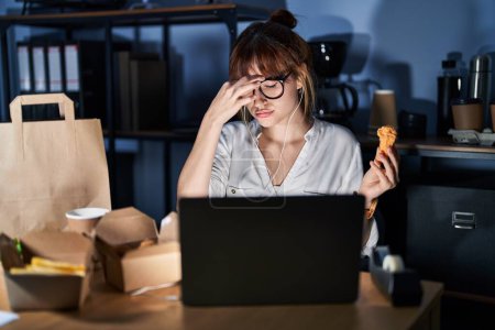 Foto de Young beautiful woman working using computer laptop and eating delivery food tired rubbing nose and eyes feeling fatigue and headache. stress and frustration concept. - Imagen libre de derechos