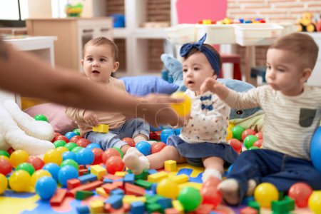 Téléchargez les photos : Groupe de tout-petits jouant avec des jouets assis sur le sol à la maternelle - en image libre de droit