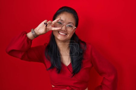 Téléchargez les photos : Asian young woman standing over red background doing peace symbol with fingers over face, smiling cheerful showing victory - en image libre de droit