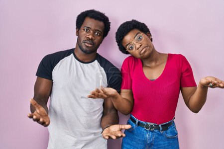 Photo for Young african american couple standing over pink background clueless and confused with open arms, no idea concept. - Royalty Free Image