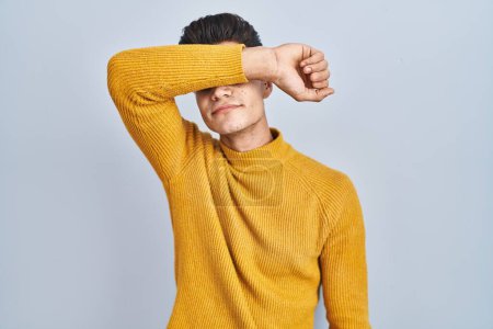 Photo for Young hispanic man standing over blue background covering eyes with arm, looking serious and sad. sightless, hiding and rejection concept - Royalty Free Image