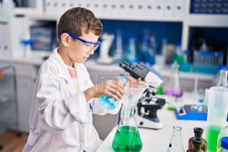 Foto de Niño rubio vistiendo uniforme científico midiendo líquido en laboratorio - Imagen libre de derechos