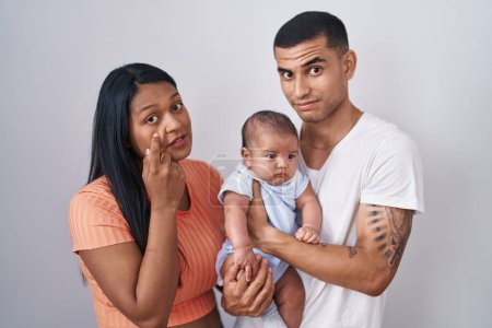 Photo for Young hispanic couple with baby standing together over isolated background pointing to the eye watching you gesture, suspicious expression - Royalty Free Image