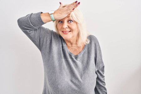 Foto de Middle age caucasian woman standing over white background surprised with hand on head for mistake, remember error. forgot, bad memory concept. - Imagen libre de derechos