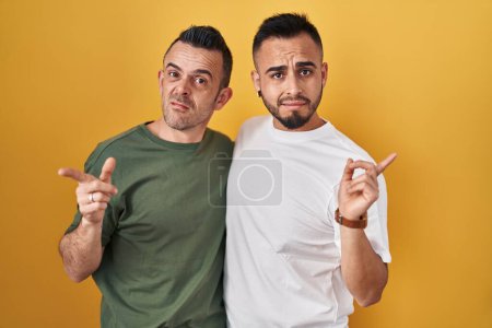 Téléchargez les photos : Couple homosexuel debout sur fond jaune pointant de côté inquiet et nerveux avec index, expression inquiète et surprise - en image libre de droit