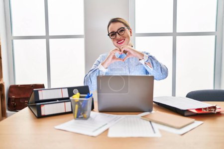 Photo for Young hispanic woman working at the office wearing glasses smiling in love showing heart symbol and shape with hands. romantic concept. - Royalty Free Image