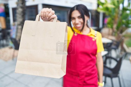 Téléchargez les photos : Jeune belle serveuse arabe souriante confiante tenant à emporter de la nourriture à la terrasse du café - en image libre de droit