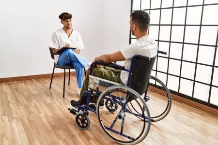 Photo for Two hispanic men physiotherapist and patient sitting on wheelchair having rehab session at clinic - Royalty Free Image
