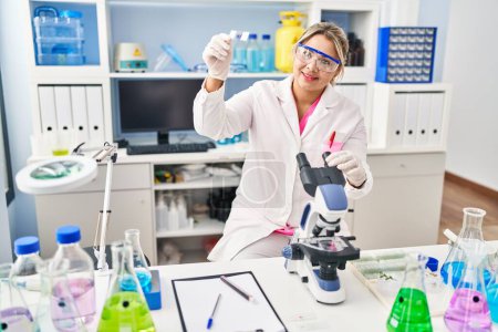 Téléchargez les photos : Jeune femme hispanique portant l'uniforme de scientifique utilisant le microscope au laboratoire - en image libre de droit