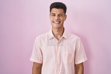 Photo for Young hispanic man standing over pink background winking looking at the camera with sexy expression, cheerful and happy face. - Royalty Free Image