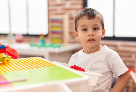 Foto de Adorable niño jugando con bloques de construcción sentado en la mesa en el jardín de infantes - Imagen libre de derechos
