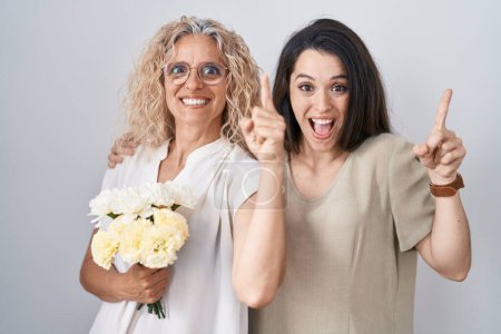 Téléchargez les photos : Mère et fille tenant un bouquet de fleurs blanches souriant étonné et surpris et pointant vers le haut avec les doigts et les bras levés. - en image libre de droit
