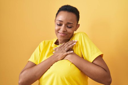 Photo for African american woman smiling confident with hands on heart over isolated yellow background - Royalty Free Image