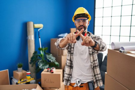 Téléchargez les photos : Young hispanic man with beard working at home renovation rejection expression crossing fingers doing negative sign - en image libre de droit