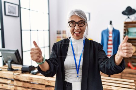 Photo for Middle age grey-haired woman working as manager at retail boutique success sign doing positive gesture with hand, thumbs up smiling and happy. cheerful expression and winner gesture. - Royalty Free Image