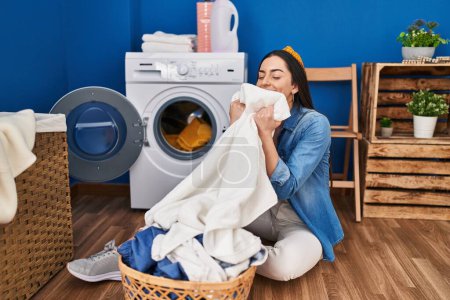 Photo for Young beautiful hispanic woman smiling confident smelling clean clothes at laundry room - Royalty Free Image
