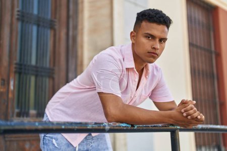 Téléchargez les photos : Jeune homme latin avec une expression détendue penché sur la balustrade à la rue - en image libre de droit
