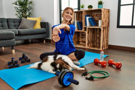 Photo for Young caucasian woman stretching arms sitting on floor with dog at home - Royalty Free Image