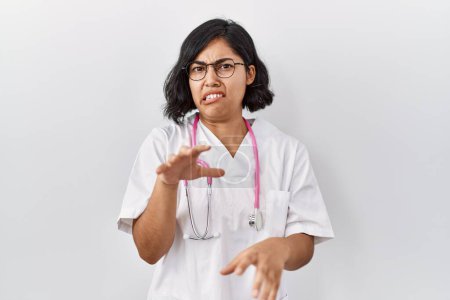 Téléchargez les photos : Young hispanic doctor woman wearing stethoscope over isolated background disgusted expression, displeased and fearful doing disgust face because aversion reaction. with hands raised - en image libre de droit