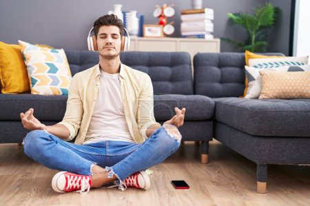 Photo for Young hispanic man doing yoga exercise sitting on floor at home - Royalty Free Image