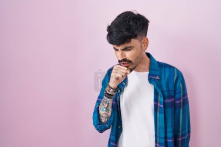 Foto de Young hispanic man with beard standing over pink background feeling unwell and coughing as symptom for cold or bronchitis. health care concept. - Imagen libre de derechos